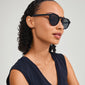 Woman wearing ALEJANDRA sunglasses black by Pilgrim, showcasing a modern round frame with angular details, embodying a trendy and confident style.
