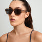Woman wearing ANNALISE sunglasses by Pilgrim, featuring an angular frame in a transparent smoky shade, ideal for beach or city outings.