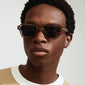ANNALISE sunglasses in a light grey, angular frame with smoky lenses, worn by a man, showcasing trendy eyewear by Pilgrim.