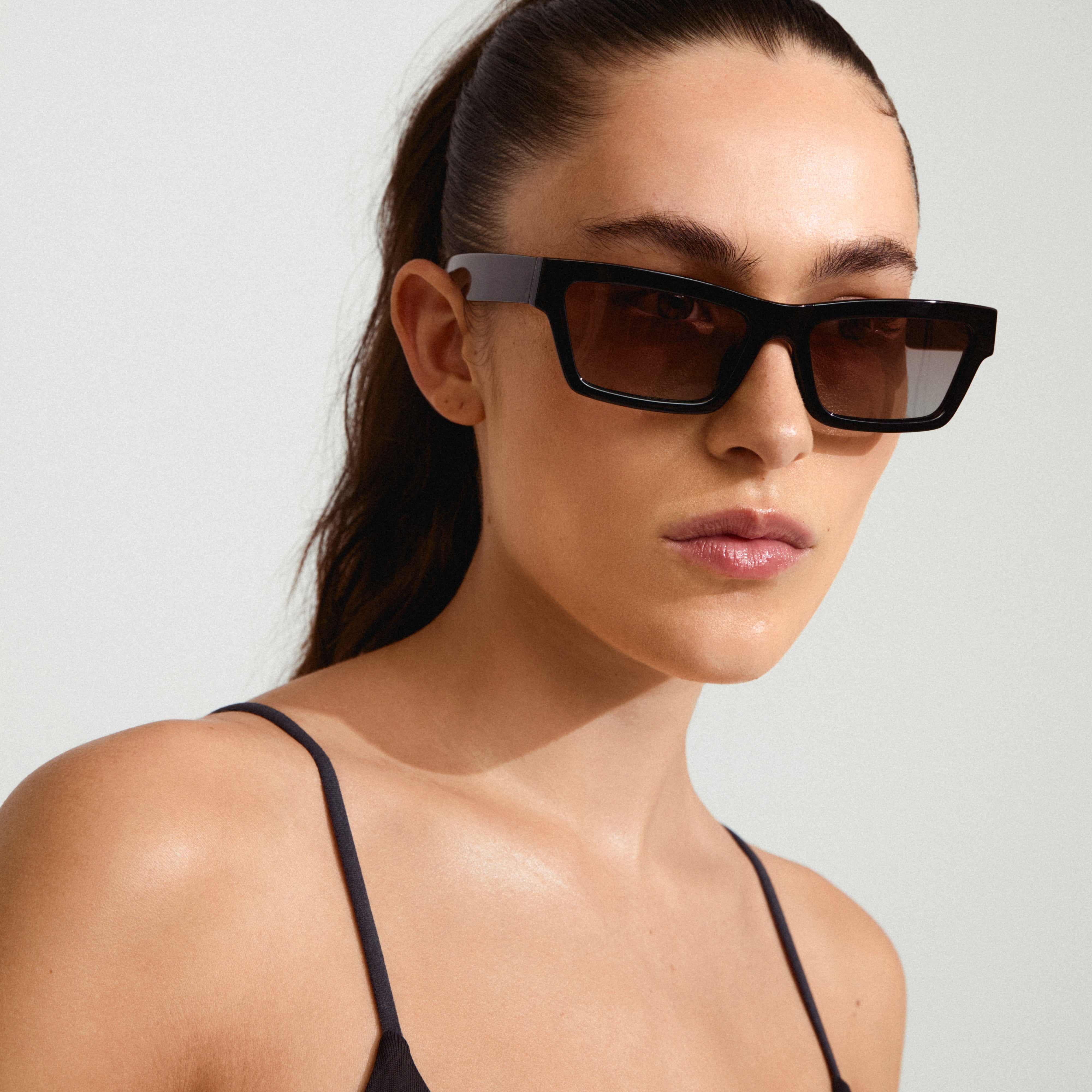 Woman wearing ASHLYN sunglasses with angular design, conveying confidence and trendiness, perfect for spring style. Sunglasses provide UVA/UVB protection, made from 75% recycled plastic.