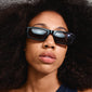 Woman with dark hair wearing ALAYNA sunglasses featuring wide chunky temples and slim, angular frames, embodying urban retro vibes from Pilgrim.