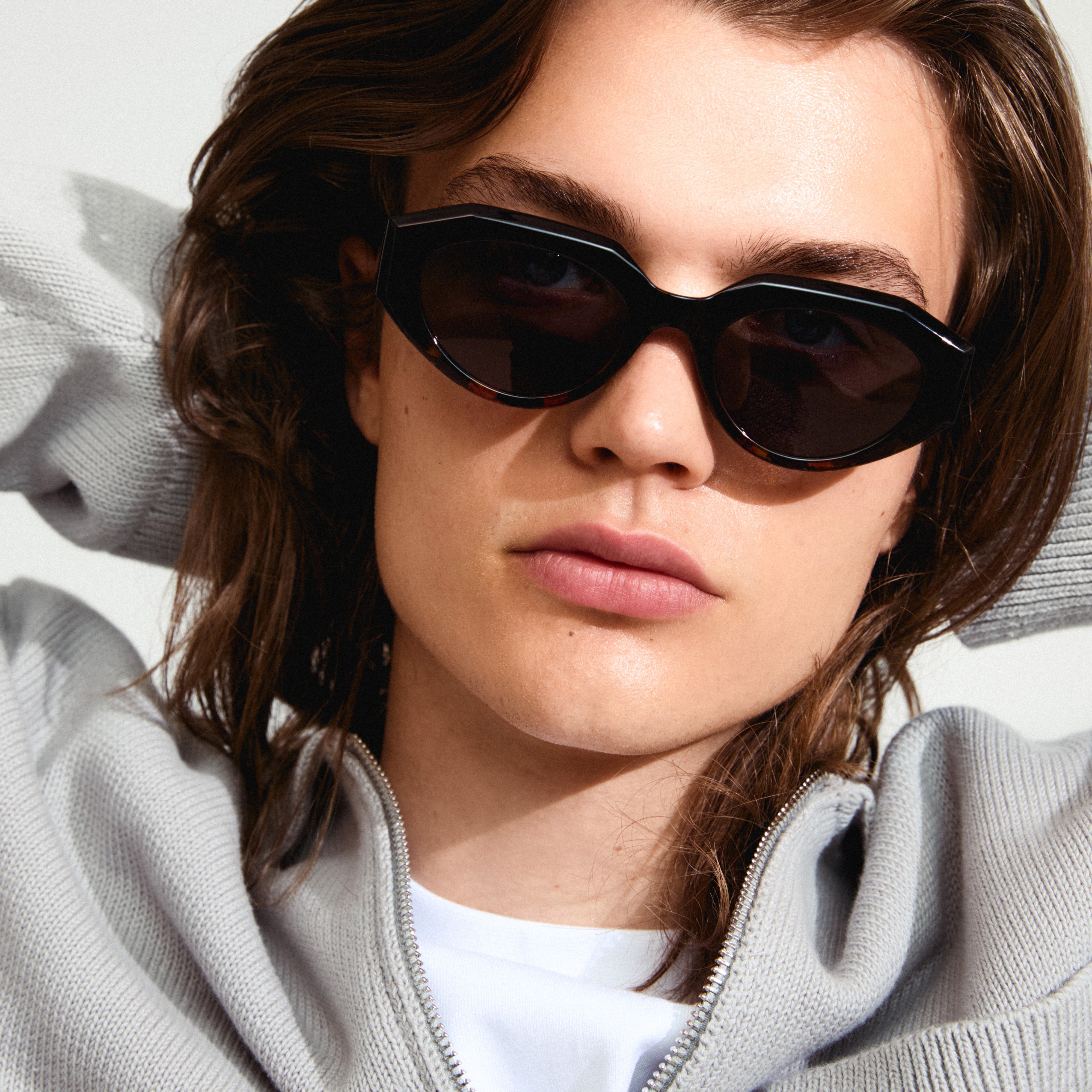 Close-up of a woman wearing Pilgrim's ALEXIS sunglasses in tortoise brown, featuring a chunky, futuristic design with UVA/UVB protection lenses.