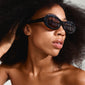 ALEXANDRIA sunglasses black by Pilgrim, featuring retro-inspired oval frames, worn by a woman with curly hair and sunglasses, highlighting fashion-forward eyewear style.