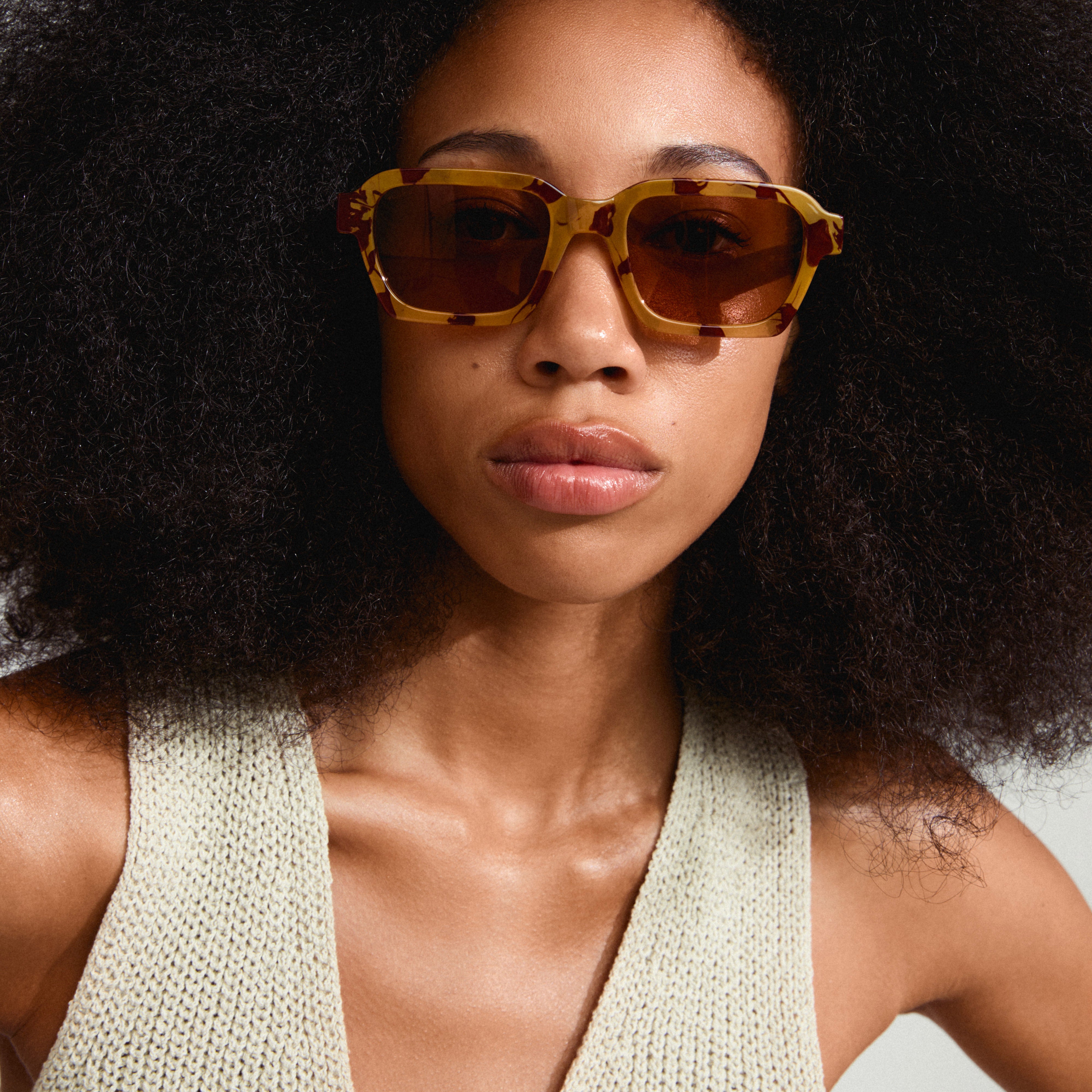 ANNALISE sunglasses tortoise brown featuring an angular frame and orange lenses, worn by a woman with an afro hairstyle, highlighting a trendy accessory for summer.