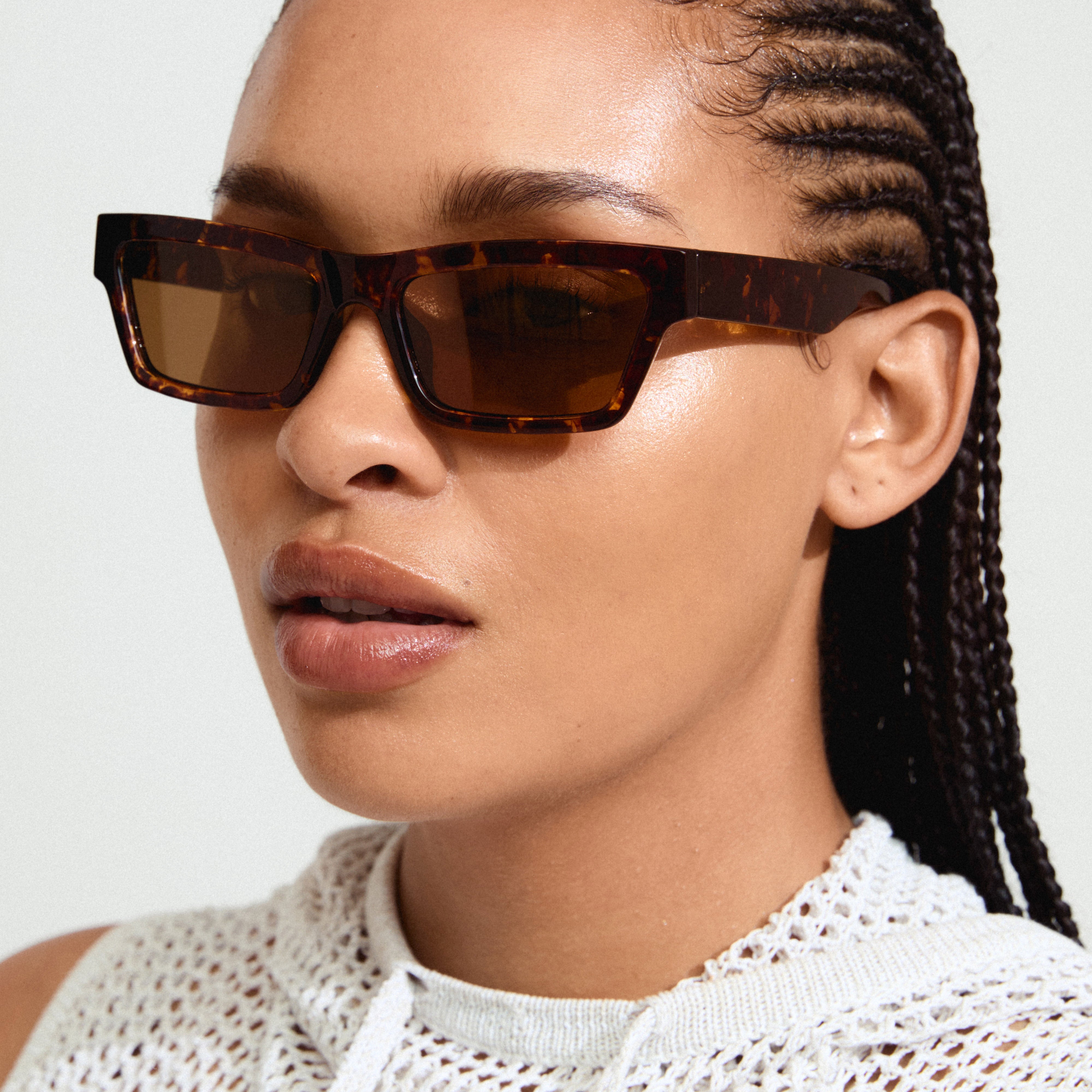 Woman wearing ASHLYN sunglasses, showcasing angular design with a confident, trendy vibe. Perfect for spring fashion, offering UV protection and eco-friendly materials.