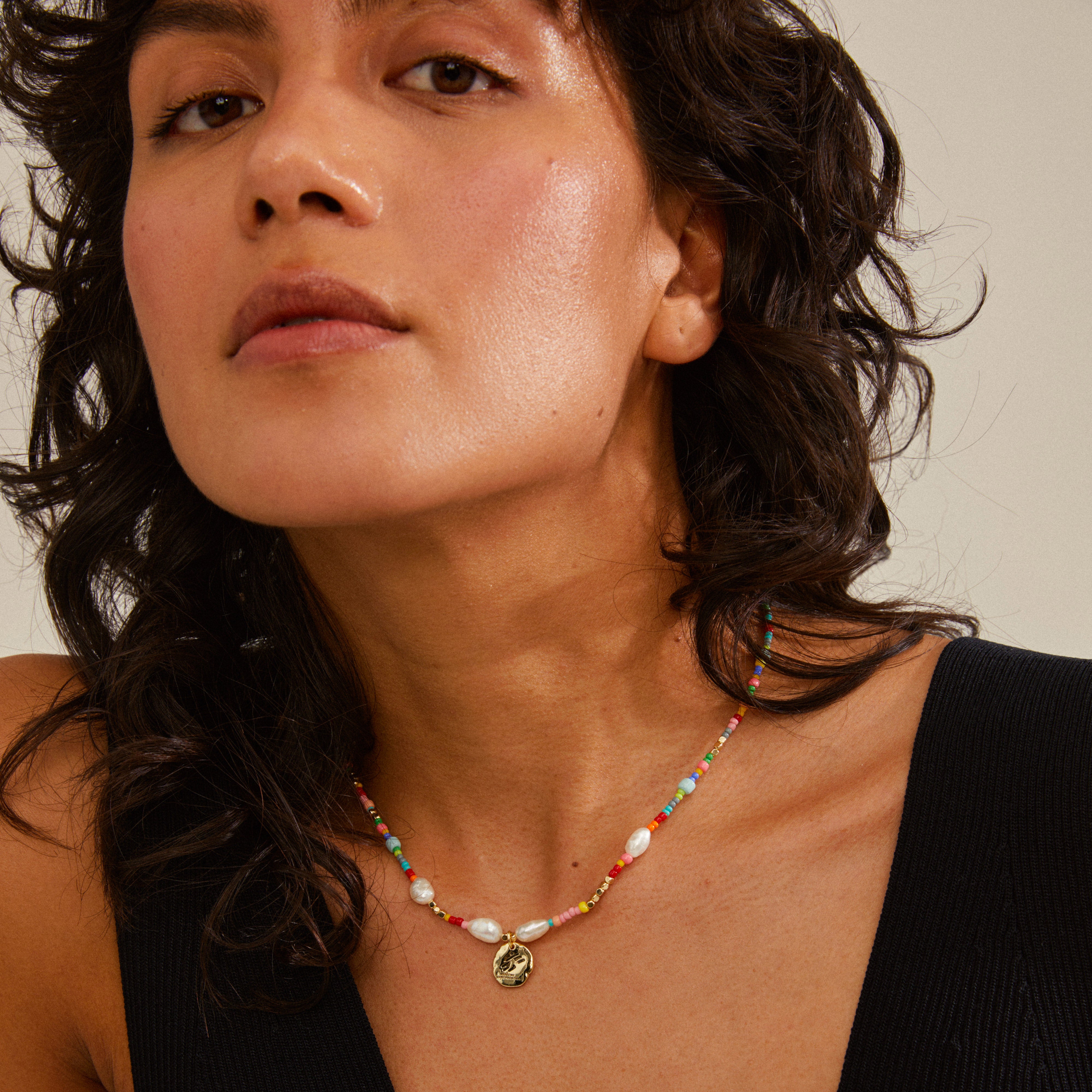 MSF necklace multi-coloured/gold-plated on a woman with curly hair, featuring a gold-plated coin pendant engraved with the MSF logo.