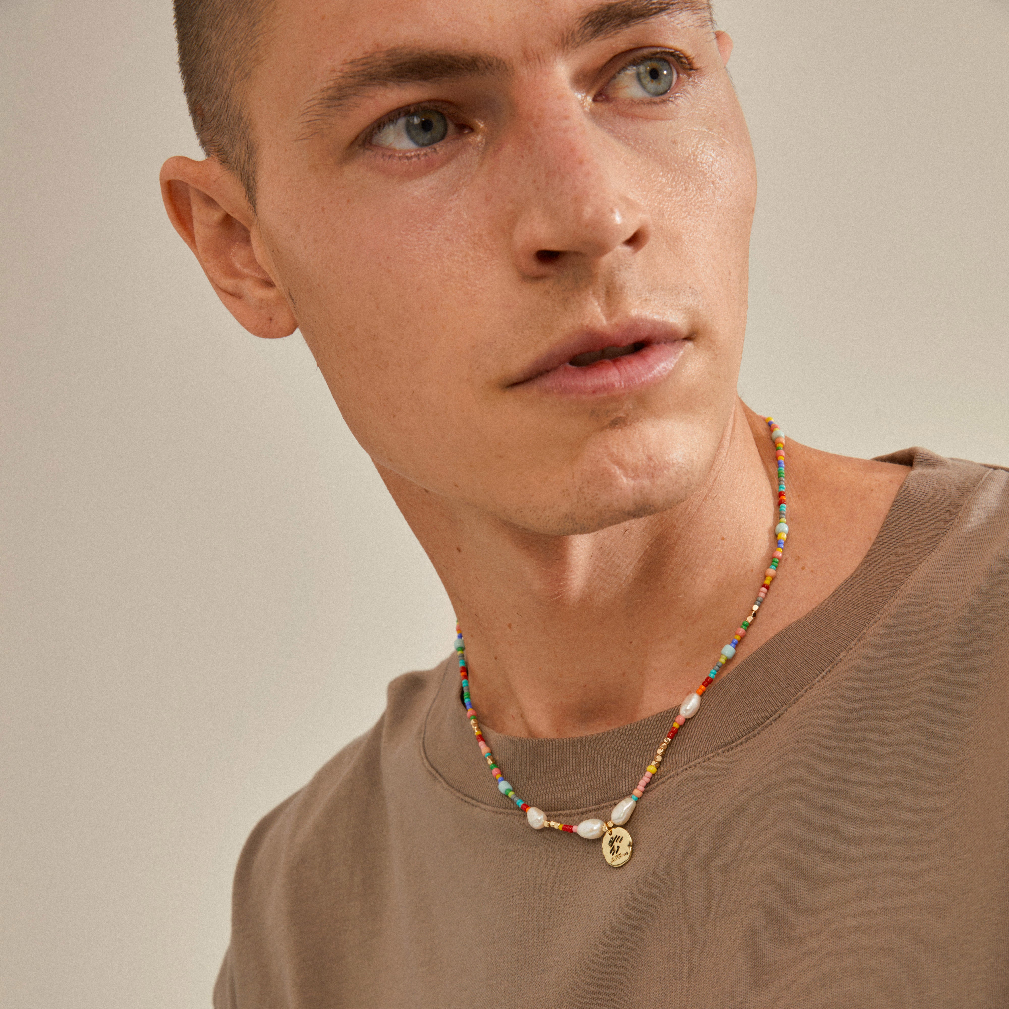 Man wearing the MSF necklace, featuring a gold-plated coin pendant with the MSF logo, highlighting its playful, supportive design.