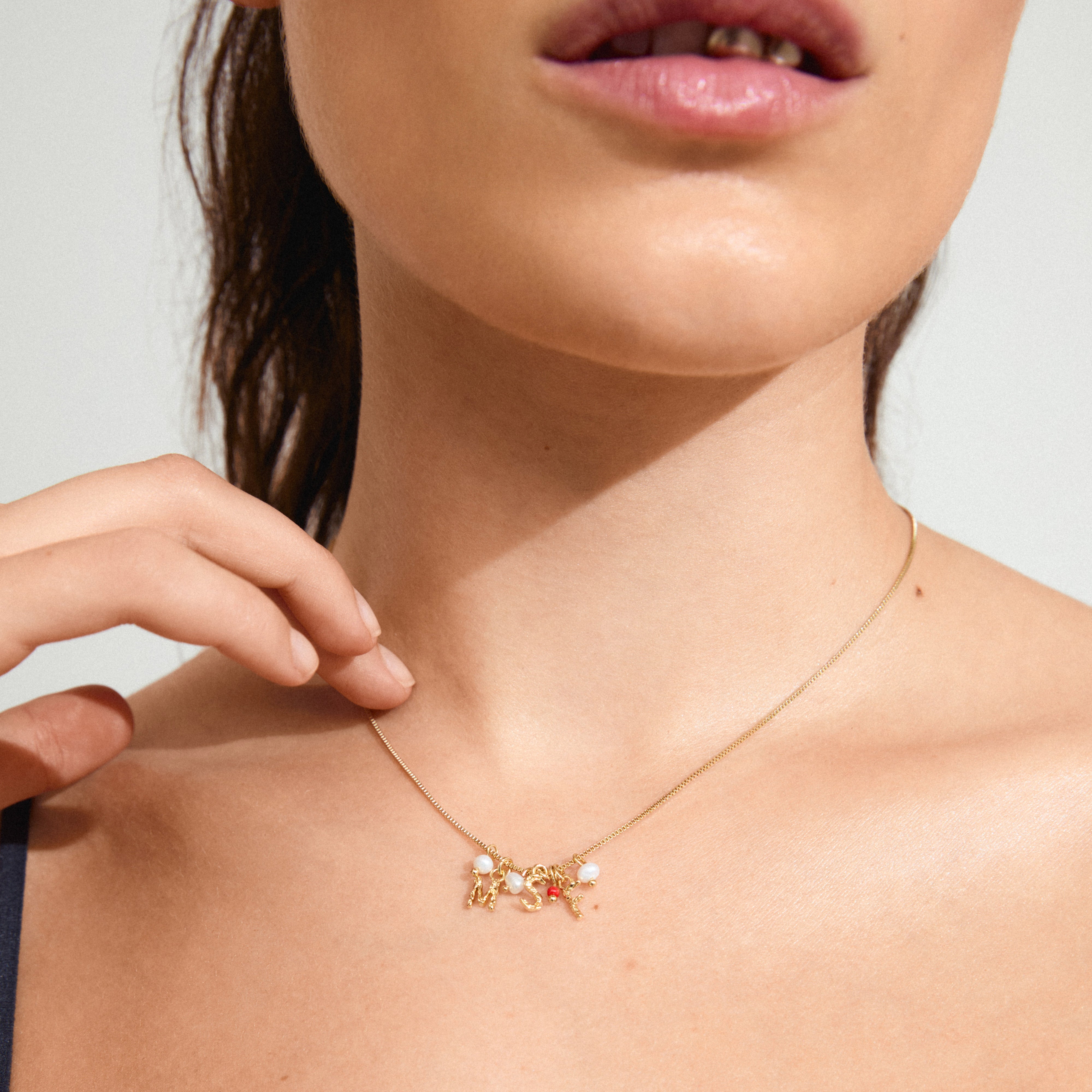 MSF charity necklace gold-plated, adorned with gold letters, freshwater pearls, and a red micro pearl, symbolizing support for Doctors Without Borders.