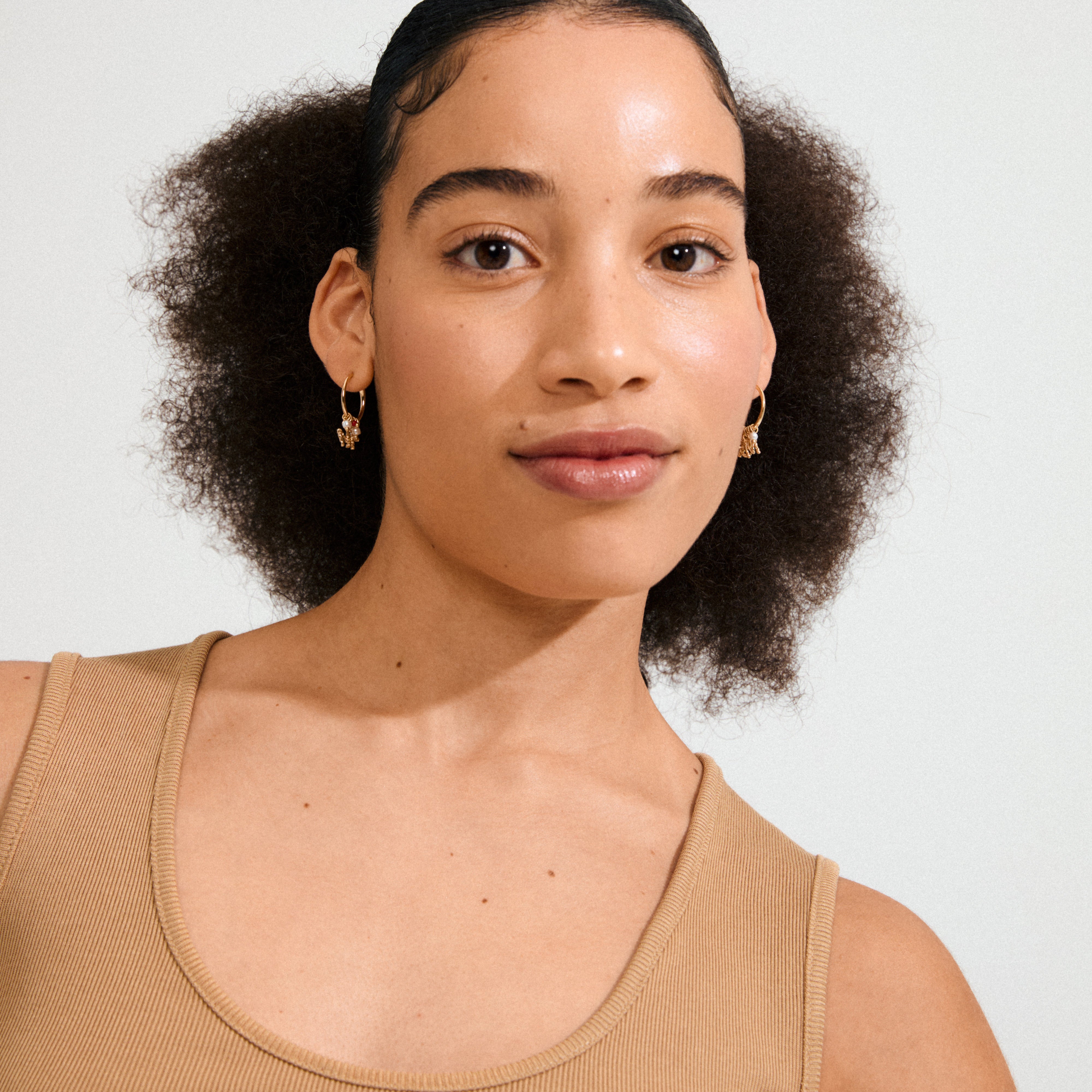 Young woman wearing MSF earrings gold-plated with dangling red bead and pearly charms, showcasing a trendy and meaningful style.