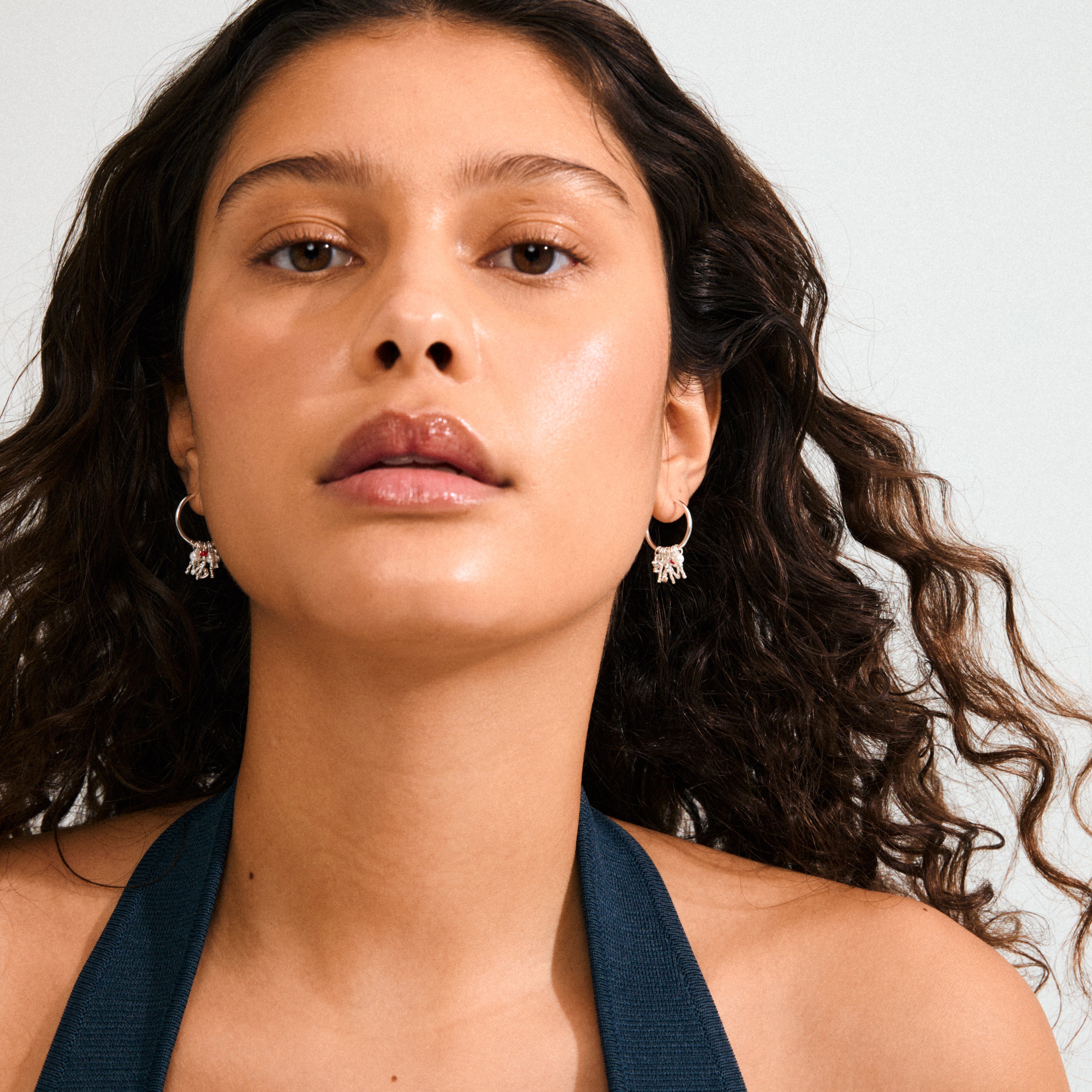 Young woman wearing MSF earrings, silver-plated hoops with dangling MSF pendants, red and white glass beads, styled for a trendy, impactful look supporting Doctors Without Borders.