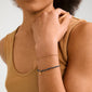 Person wearing the BELLAMY gift set, featuring a twisted gold-plated chain bracelet and a bead bracelet with a gold charm, on their wrist.