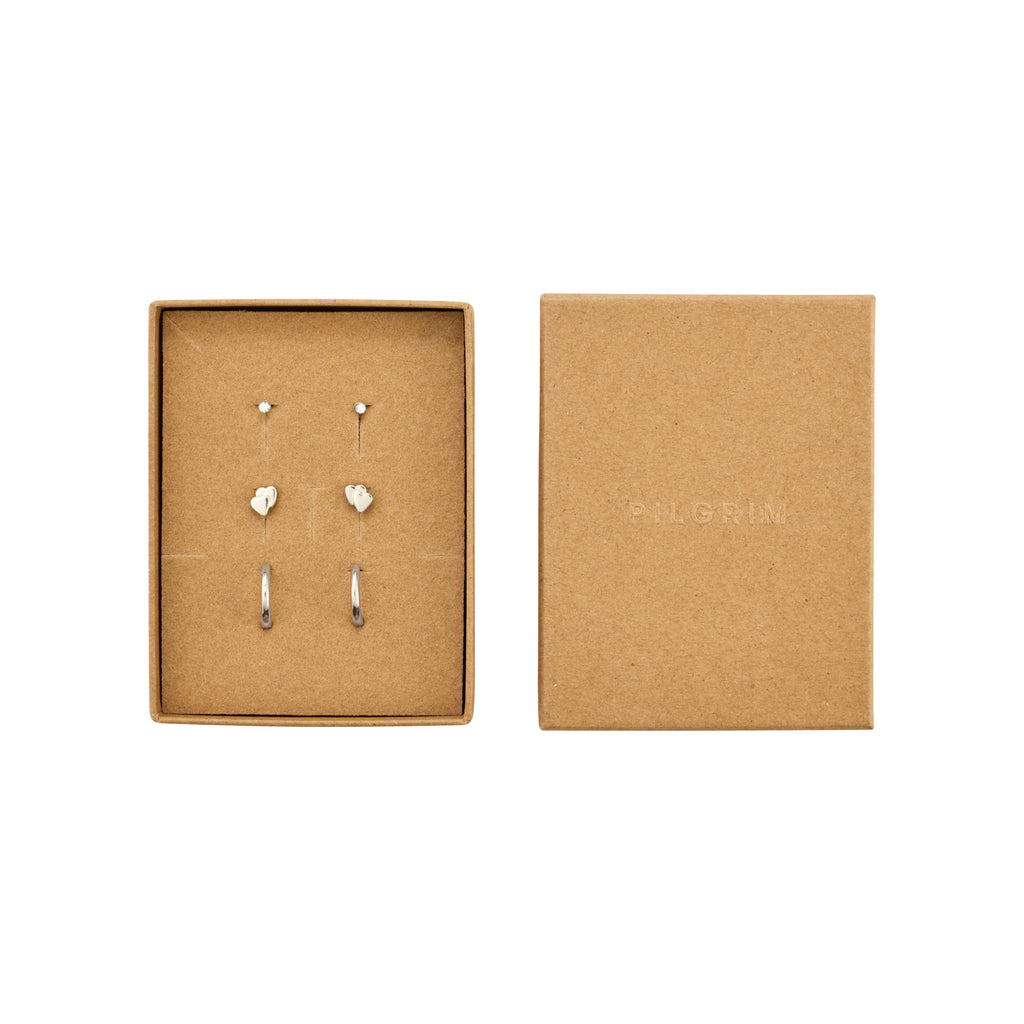 PILGRIM HALO gift set: Three pairs of silver-plated earrings, featuring crystal studs, heart studs, and huggie hoops in an open brown-kraft jewelry box.