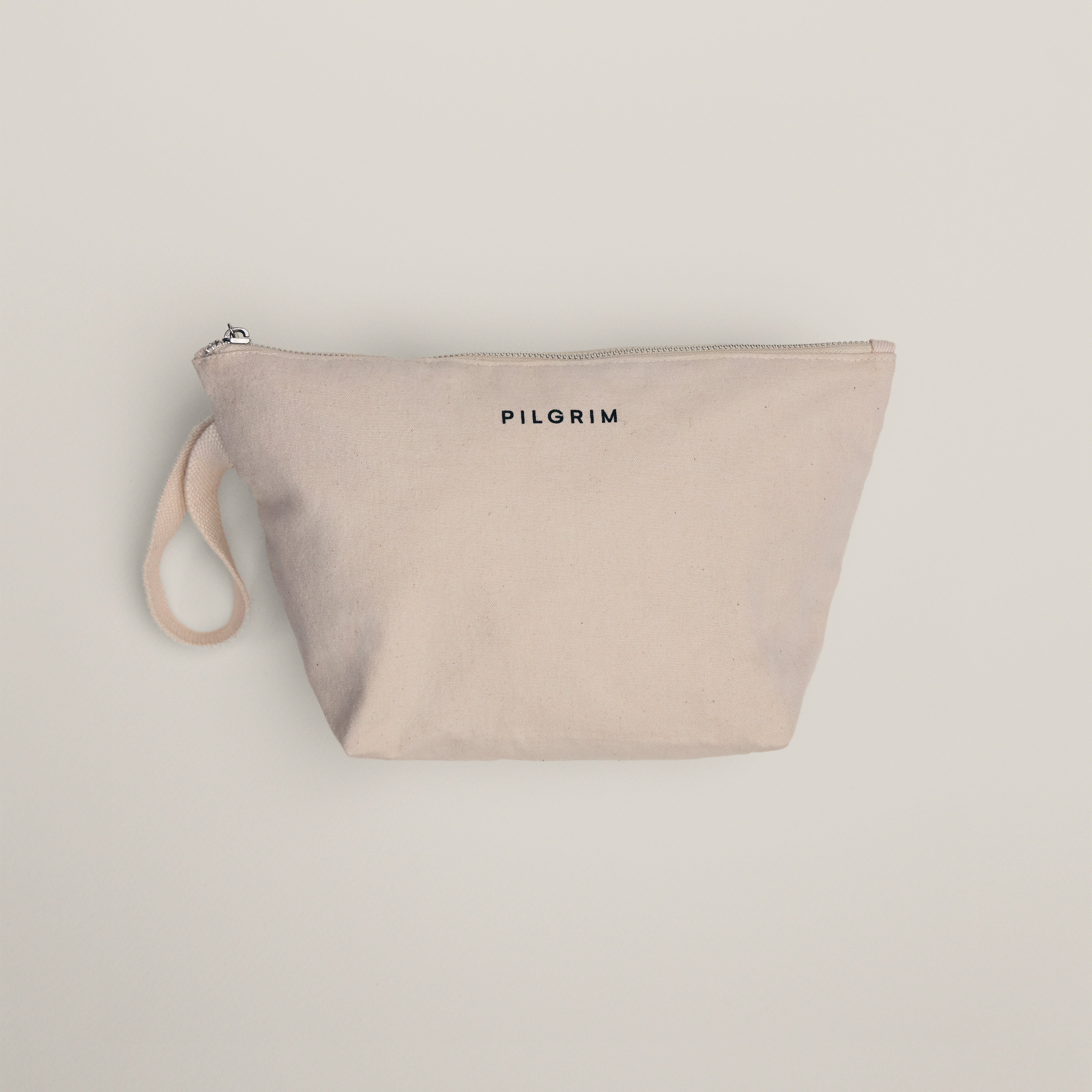 Light-beige canvas pouch with PILGRIM printed on front, featuring a zipper and fabric loop, designed to hold a gold-plated hoops set and foldable mirror.