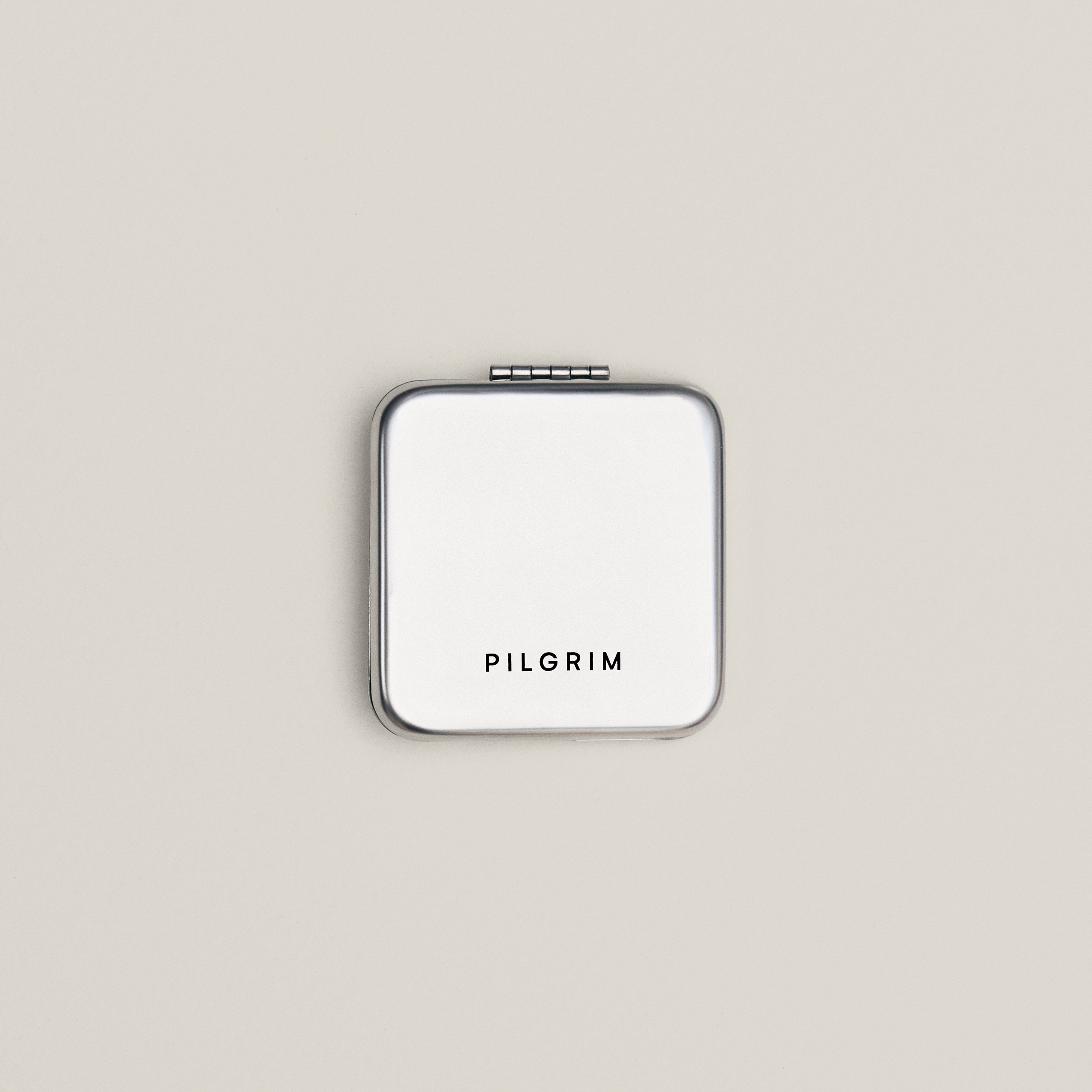 Silver compact case with PILGRIM branding, part of the Limited Goodie Bag featuring gold-plated hoops and a foldable mirror in a soft cotton pouch.