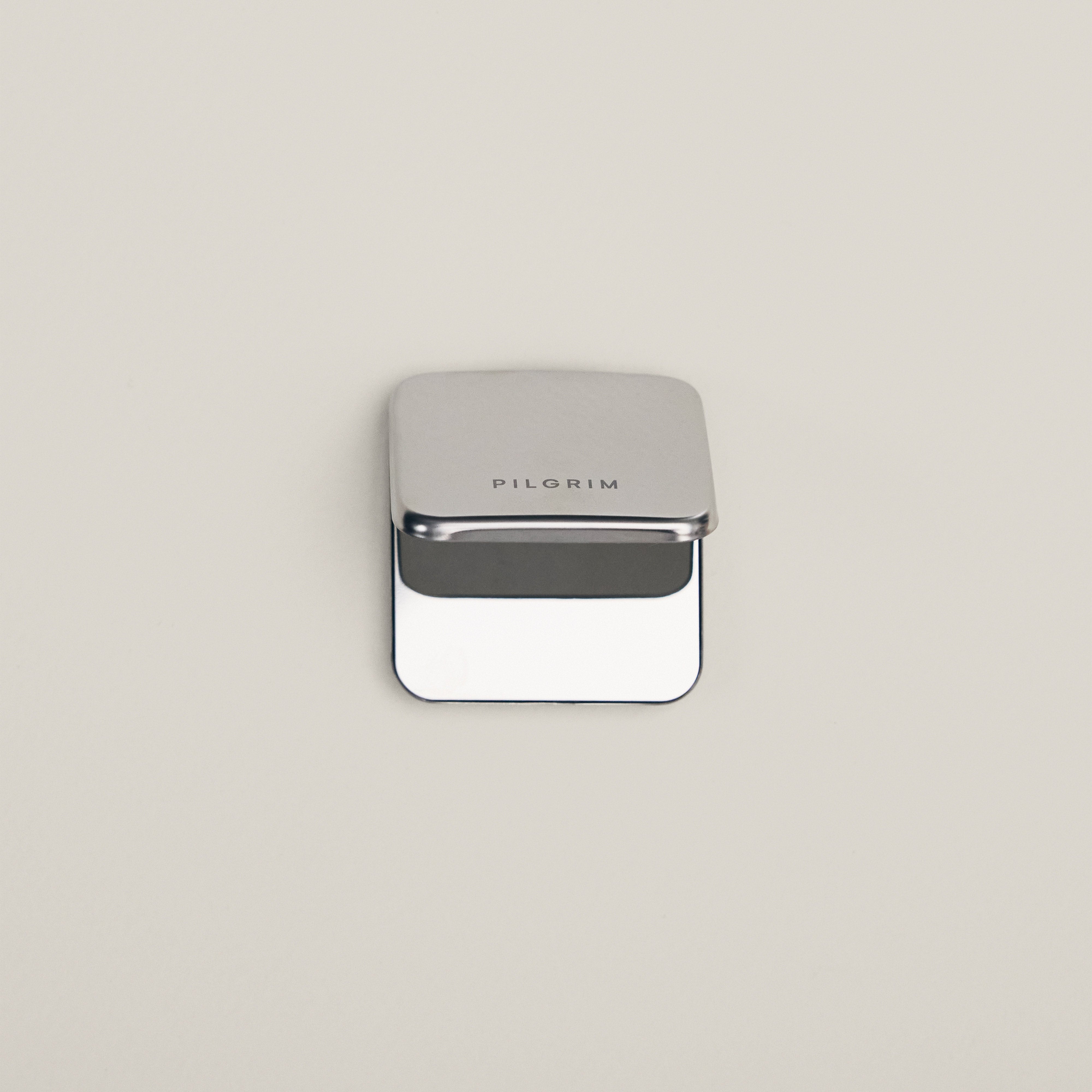 Silver-toned metal box with PILGRIM on the lid, open to reveal space for storing the Limited Goodie Bag’s gold-plated hoops and foldable mirror.