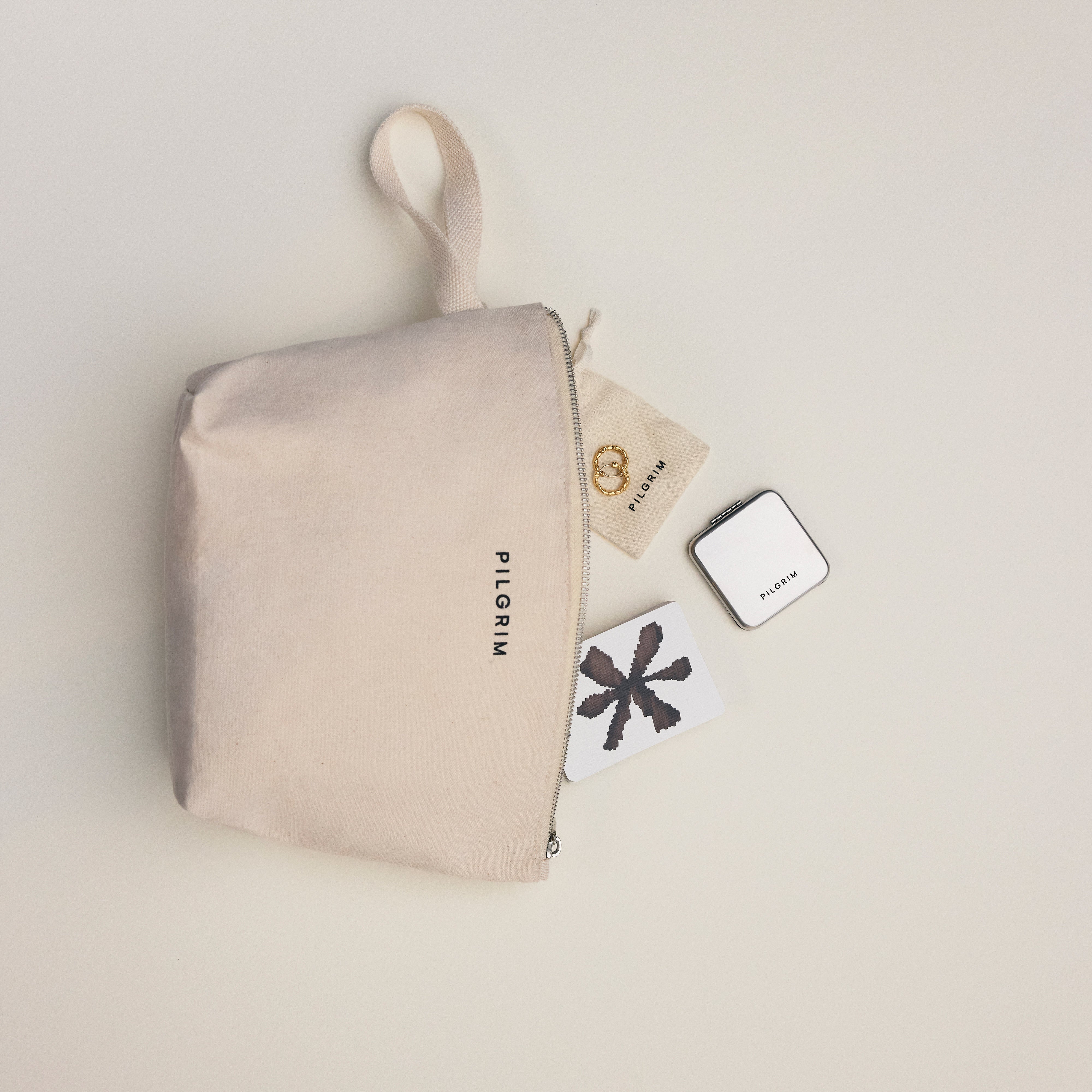 Limited Goodie Bag featuring a natural-canvas pouch with gold-plated hoops and a compact mirror, all branded “PILGRIM” and arranged neatly.
